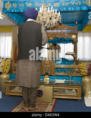 Sikh priest Garanthi Jarnail Singh prays with eyes closed and holding a microphone in front of the Granth, the sacred scripture of Sikhism, in Munich, Germany, 22 March 2009. Turban, beard and bracelet are the visible signs of being a Sikh, taking off shoes in the temple and abdication of indulgence food are established rules of the Sikh. Sikhism denies the worshipping of gods resp Stock Photo