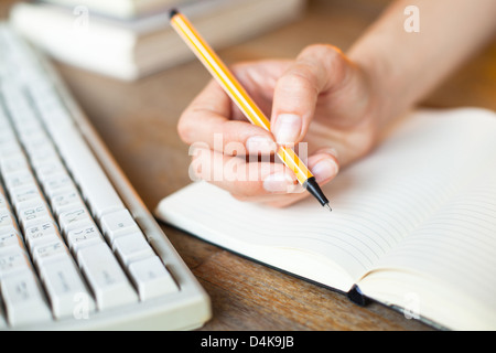 Hands writes in a notebook, keyboard, a stack of books in background Stock Photo