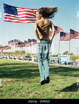 Woman jumping in field of US flags Stock Photo