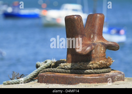 A heavy metal iron steel mooring cleat with a boat yacht dingy tied up rope wrapped around on a pier peir harbor harbour quay Stock Photo