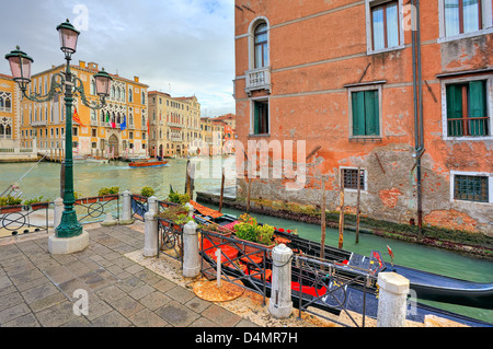 Two gondolas on narrow canal between red brick house and small plaza with lamppost as Grand Canal on background in Venice. Stock Photo