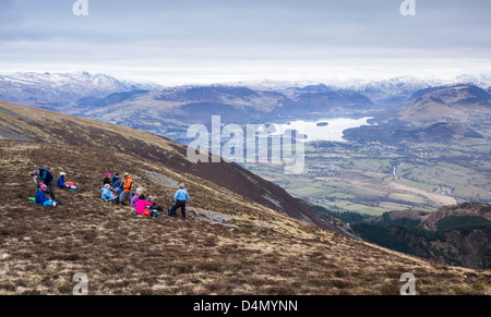 Hikers stop for a rest at Long Side on the way to the summit of Skiddaw with Derwent Water in  the distance. Stock Photo