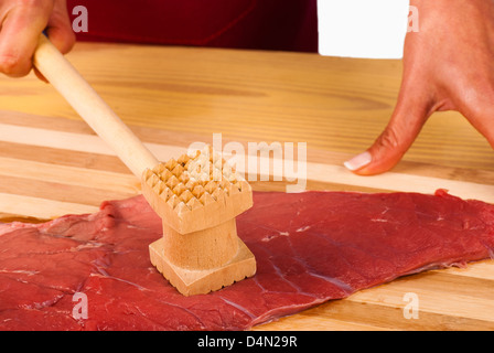 Hands tenderizing meat with a kitchen hammer Stock Photo