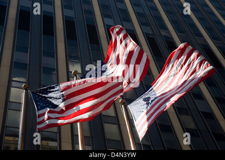 Three US stars and stripes flags flying in the wind in front of a skyscraper in New York, USA Stock Photo