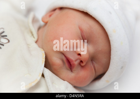 Newborn sleeping baby girl wrapped in a fleece bodysuit and hat. Taken at precisely 2 hours old. Focus on eye. Stock Photo