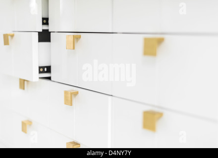 Rows of white sleek drawers with golden handles in strict geometric style. Two half-opened drawers in background. House or offic Stock Photo