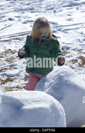 Child toddler baby blond girl walking and playing in snowy landscape - winter mountain Stock Photo