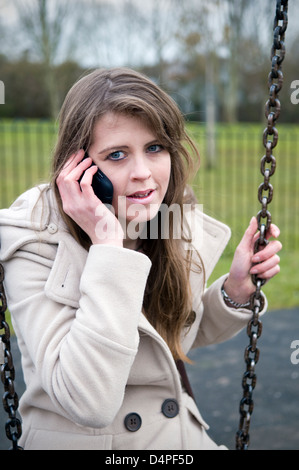 Attractive young Caucasian woman talking on mobile on swing in park in Bristol, uk Stock Photo