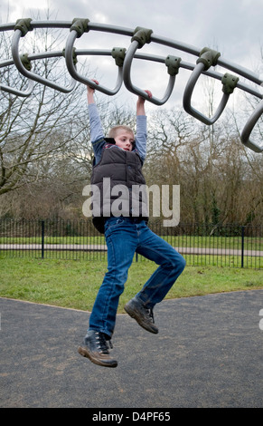 Young 10 year old Caucasian boy swinging across climbing frame in park in Bristol, UK Stock Photo