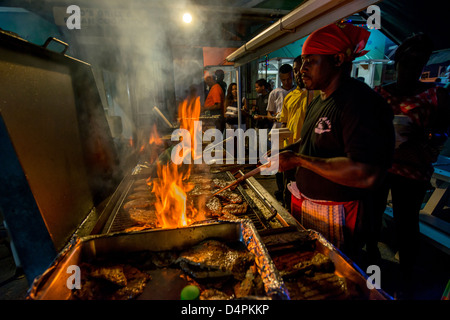 A man frying up fish on a BBQ at Oistins fish fry night, Oistins, parish of Christ Church, Barbados , Caribbean, West Indies Stock Photo