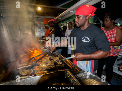 A man frying up fish on a BBQ at Oistins fish fry night, Oistins, parish of Christ Church, Barbados , Caribbean, West Indies Stock Photo