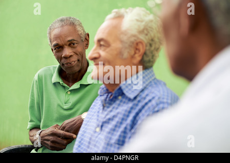 three senior men sitting on bench in park and talking Stock Photo