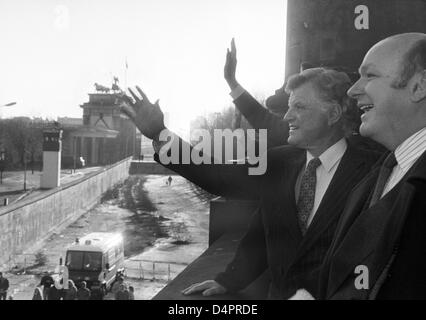 (dpa file) A file picture dated 28 November 1989 captures U.S. Senator Ted Kennedy (C) and Berlin?s then governing lord mayor Walter Momper, glance at the Berlin Wall and Brandenburg Gate and wave at GDR border guards in Berlin, Germany. Kennedy visited Berlin on the occasion of the opening of the Berlin Wall. Photo: Wolfgang Kumm Stock Photo
