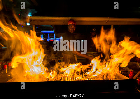 A man frying up fish on a BBQ at Oistins fish fry night, Oistins, parish of Christ Church, Barbados , Caribbean, West Indies Stock Photo