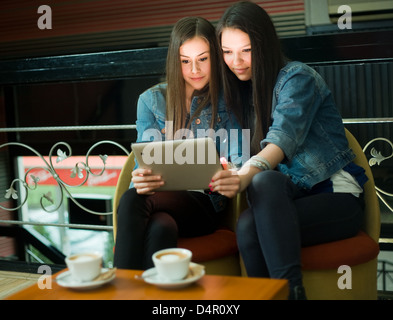 Two cute teen girls having fun with tablet computer in coffe shop. Stock Photo
