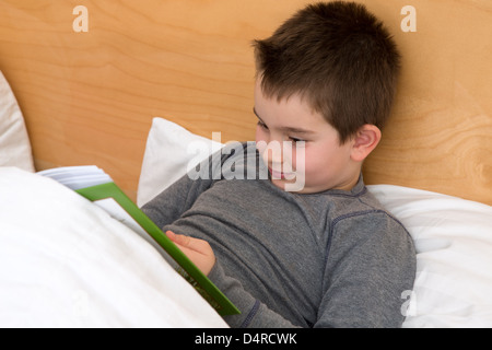 Eight years old reading his book in the bed before he goes to sleep. Stock Photo