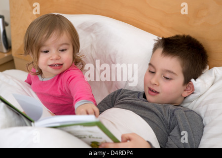 Little sister pointing a page to his older brother in the book before they go to sleep. Stock Photo