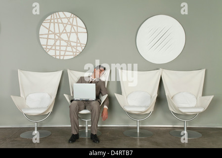 Young businessman fell asleep in chair with laptop computer on lap Stock Photo