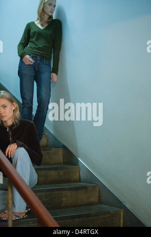 Teen girl sitting on stairs, young woman leaning on wall behind her Stock Photo