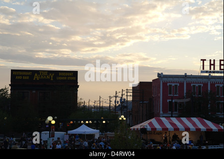 Twilight sunset view The Wrangler and Albany Liquor Mart rising above music tents and people, Cheyenne Depot Plaza, Wyoming, USA Stock Photo