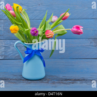 Bouquet of colorful tulips in a blue jug on blue wooden table Stock Photo