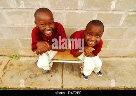 Burundi, Bujumbura, high angle view of school boys sitting on chair and smiling by school wall. (MR) Stock Photo