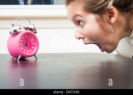 Close up as a young woman gapes at a pink alarm clock in shocked panic Stock Photo
