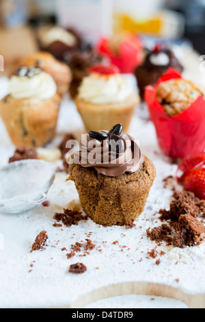 A chocolate coffee muffin surrounded by crumbs with other muffins in background Stock Photo