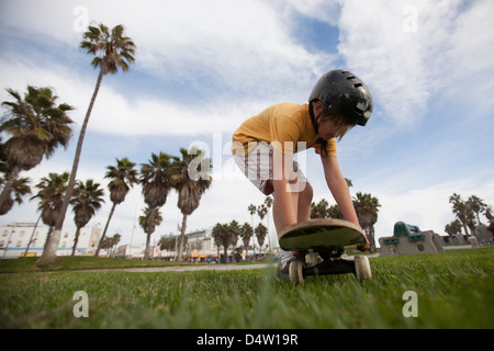 Boy putting skateboard in grass at park Stock Photo