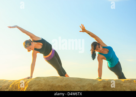 Women practicing yoga on rock formation Stock Photo