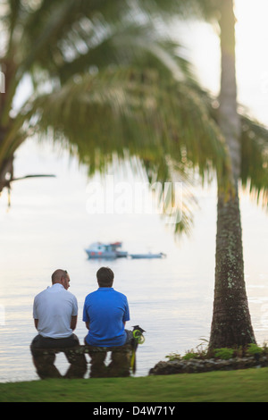 Men sitting under palm tree on beach Stock Photo