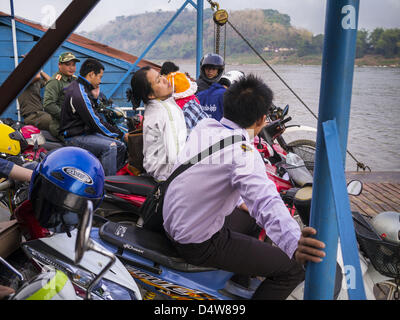 March 11, 2013 - Luang Prabang, Luang Prabang, Laos - A woman balances her child on her motorcycle while she rides a ferry across the Mekong River near Luang Prabang. The Mekong River ferries are disappearing as bridges across the river are completed and roads along the river are paved. The paving of Highway 13 from Vientiane to near the Chinese border has changed the way of life in rural Laos. Villagers near Luang Prabang used to have to take unreliable boats that took three hours round trip to get from the homes to the tourist center of Luang Prabang, now they take a 40 minute round trip bus Stock Photo