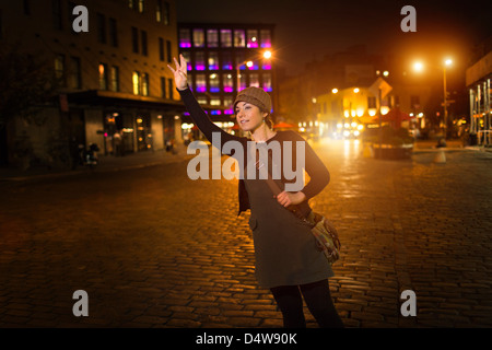 Woman hailing taxi on city street Stock Photo