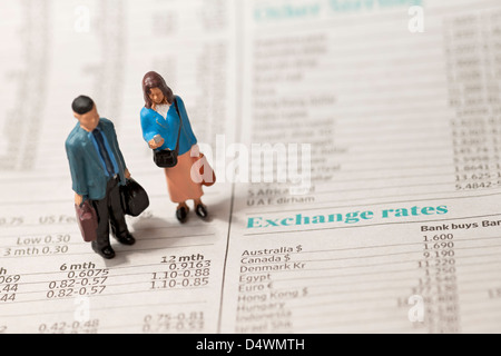 Close up of toy tiny small figure figures of a man and woman couple stood on financial page of newspaper business finance concept male female Stock Photo