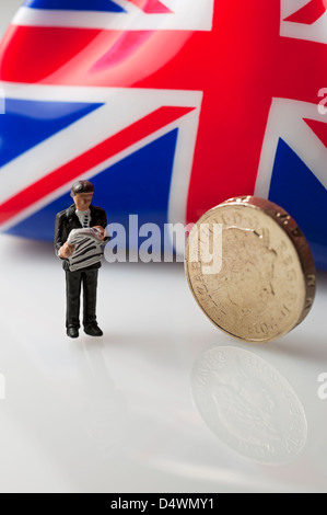 Close up of Toy tiny small figure of a businessman male person man stood next to an English pound Sterling coin money business finance concept Stock Photo