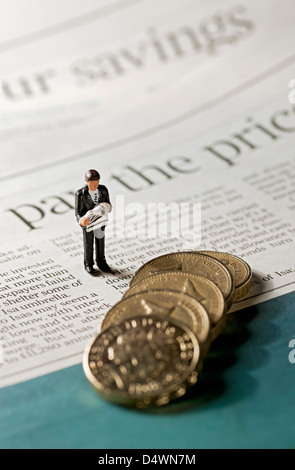 Close up of Toy tiny figure of a man stood next to English pound coins on page of financial newspaper business finance concept