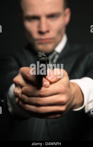 Man in suit shooting with gun. Studio shot against black. Stock Photo
