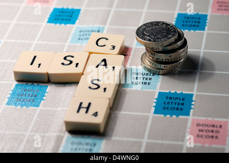 Close up of Scrabble board word words spelling Cash ISA and pile of English pound coins money business finance saving savings concept Stock Photo