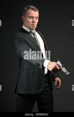 Man in suit shooting with gun. Smoking cigarette. Studio shot. Stock Photo