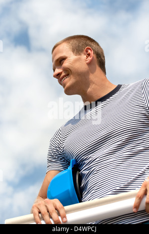Young male architect holding blueprints and smiling Stock Photo