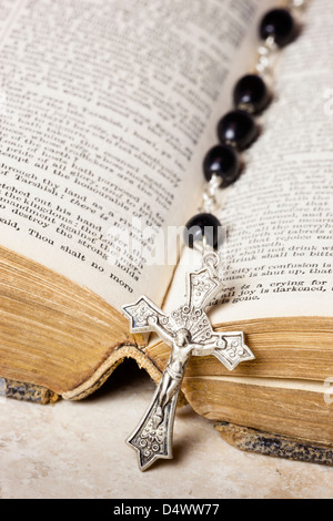 Rosary beads and cross lying on an open page of the bible. Stock Photo