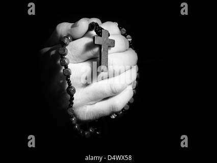 Hands holding onto rosary beads and cross while praying. Stock Photo