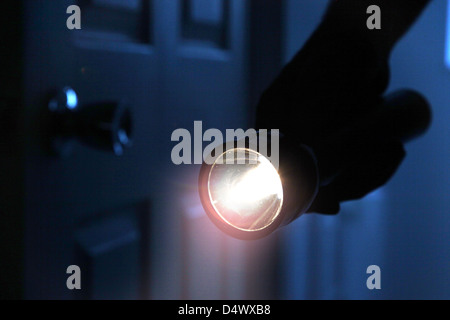 Shadowy male intruder holding a torch or flashlight entering a dark room. Stock Photo