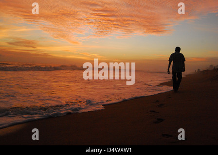 a man  walking away from a beautiful seashore after sunset,his foot prints on the sand Stock Photo