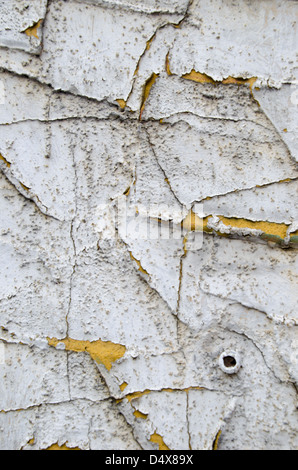 Gritty urban background texture with cracked and peeling white paint covering a yellow cement wall Stock Photo