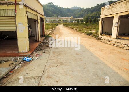 March 14, 2013 - Boten, Luang Namtha, Laos - A road going past deserted buildings leading to an abandoned Chinese hotel near the end of Highway 13 in the Boten Special Economic Zone. The SEZ is in Laos immediately south of the Lao Chinese border. It has turned into a Chinese enclave but many of the businesses struggle because their goods are too expensive for local Lao to purchase. As China's economy and its role on the world stage expands China's role in Southeast Asia is also becoming more evident. In Laos, which borders Yunnan province in southern China, the Special Economic Zone in Boten i Stock Photo