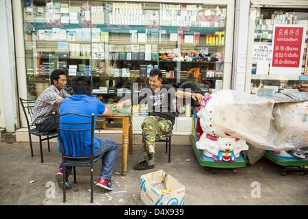 March 14, 2013 - Boten, Luang Namtha, Laos - Chinese men relax in front of a Chinese pharmacy in the Chinese market near the end of Highway 13 in the Boten Special Economic Zone. The SEZ is in Laos immediately south of the Lao Chinese border. It has turned into a Chinese enclave but many of the businesses struggle because their goods are too expensive for local Lao to purchase. As China's economy and its role on the world stage expands China's role in Southeast Asia is also becoming more evident. In Laos, which borders Yunnan province in southern China, the Special Economic Zone in Boten is es Stock Photo