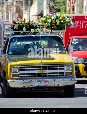 A delivery truck carries flower arrangements on the roof and a family in the cab, Oaxaca, Mexico. Stock Photo