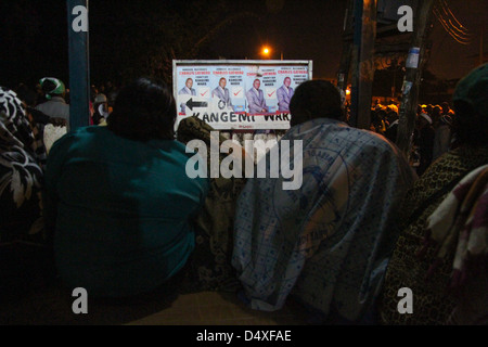 Women voters sit by campaign posters billboard at the New Kihumbuini Primary School polling station entrance. © David Mbiyu/Alamy Live News Stock Photo