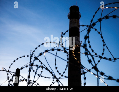 Barbed wire and dark tall industrial chimney-stalk shilouette Stock Photo